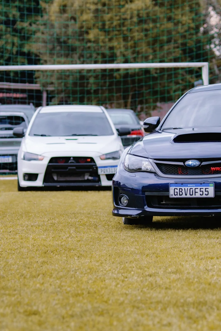 A blue Subaru WRX in the foreground, with a white Mitsubishi Lancer behind it.